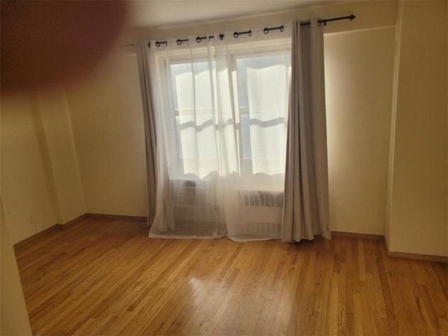 spare room featuring wood finished floors, radiator, a healthy amount of sunlight, and baseboards