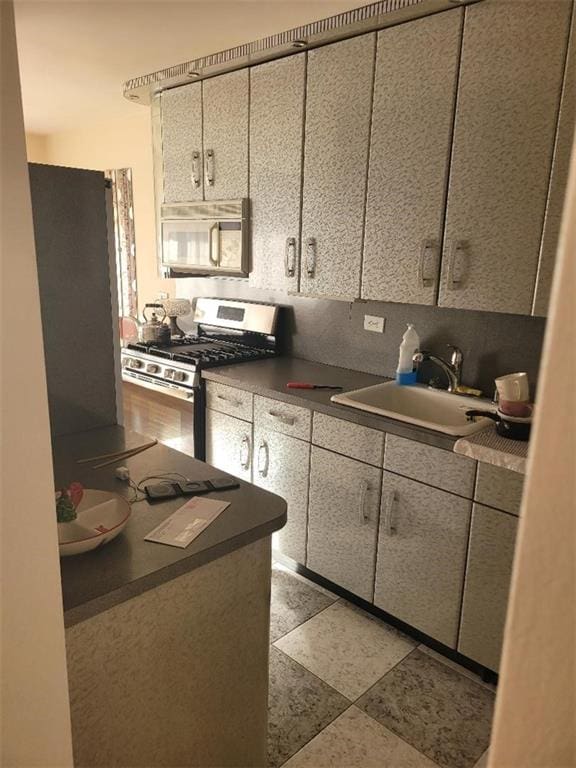 kitchen featuring dark countertops, white microwave, stainless steel gas stove, and a sink