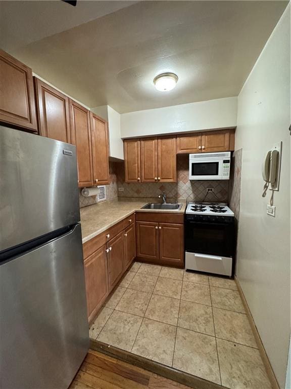 kitchen with range, white microwave, freestanding refrigerator, light countertops, and a sink