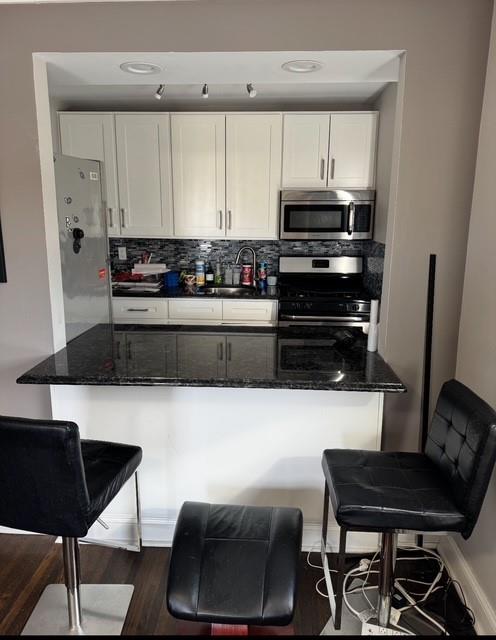 kitchen featuring dark stone countertops, stainless steel appliances, tasteful backsplash, and white cabinetry