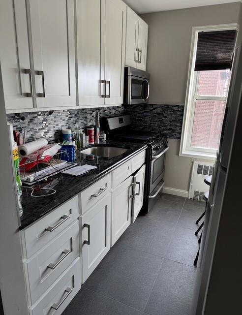 kitchen featuring backsplash, radiator, appliances with stainless steel finishes, and white cabinets