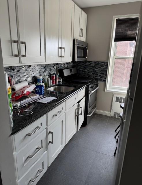 393 Avenue S Unit 5H, Brooklyn, NY 11223 - kitchen with dark tile patterned floors, stainless steel appliances, radiator heating unit, backsplash, and white cabinetry