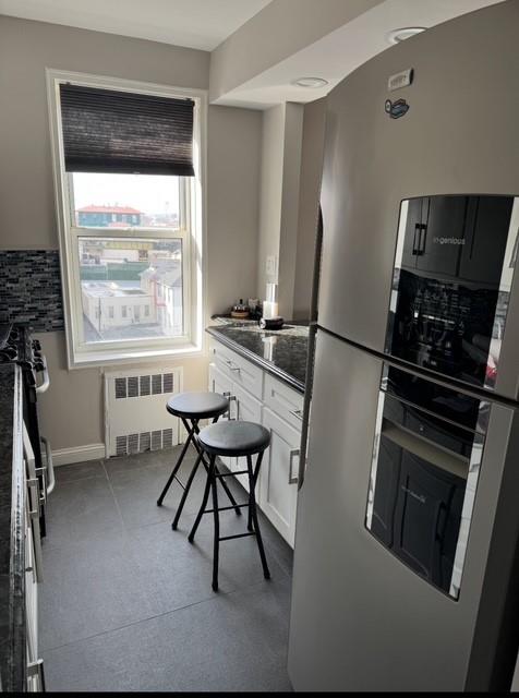 kitchen featuring dark countertops, white cabinets, radiator heating unit, and stainless steel fridge with ice dispenser