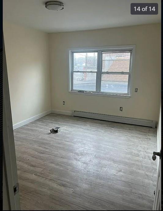 unfurnished room featuring a baseboard heating unit and light hardwood / wood-style flooring