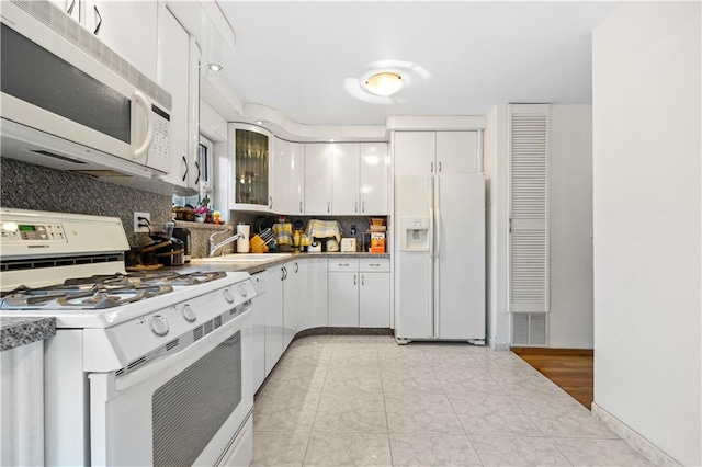 kitchen with white cabinetry, tasteful backsplash, glass insert cabinets, a sink, and white appliances