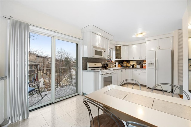 kitchen featuring a sink, light tile patterned flooring, tasteful backsplash, white cabinetry, and white appliances