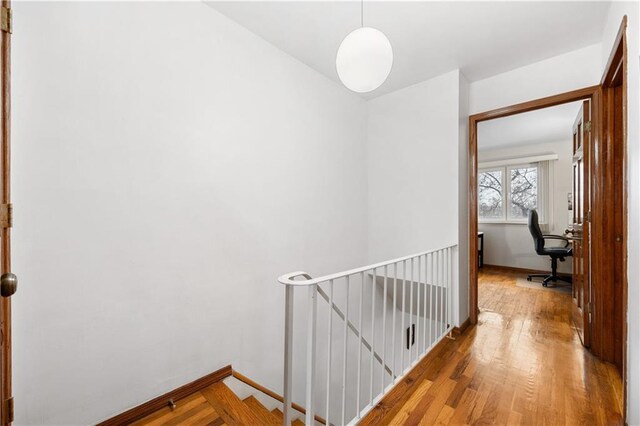 hall featuring baseboards, wood finished floors, and an upstairs landing