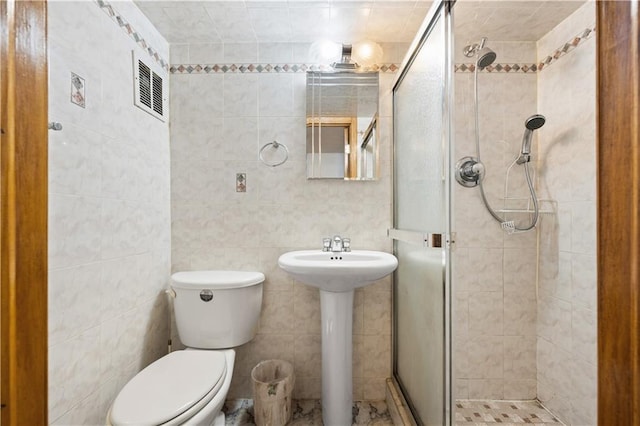 bathroom featuring tile walls, a stall shower, toilet, and a sink