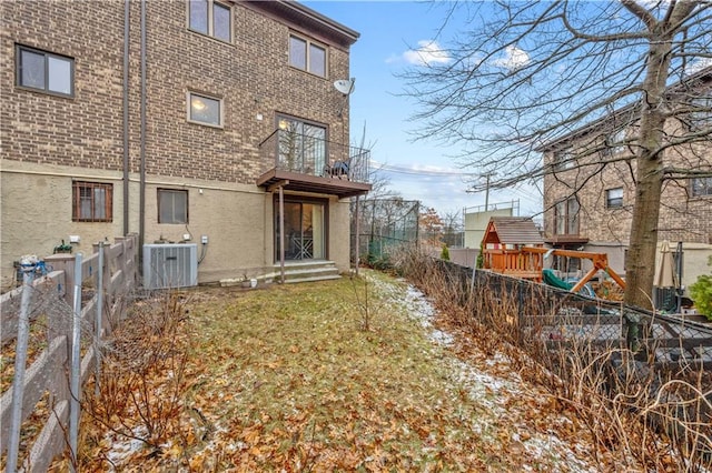 back of house featuring a fenced backyard, brick siding, central AC unit, a balcony, and a playground