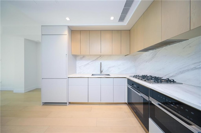 kitchen featuring sink, light hardwood / wood-style flooring, backsplash, oven, and stainless steel gas stovetop