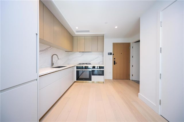 kitchen with a sink, light wood-style floors, light countertops, appliances with stainless steel finishes, and tasteful backsplash