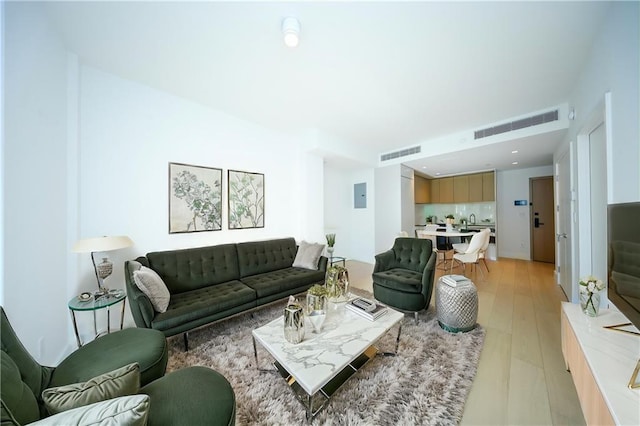 living room with light wood finished floors, visible vents, and electric panel