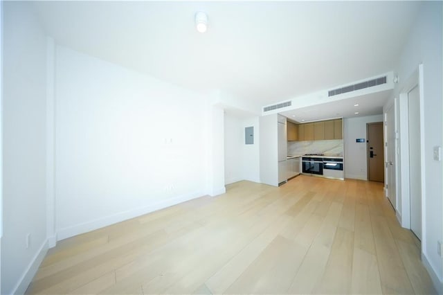 unfurnished living room featuring baseboards, light wood finished floors, visible vents, and electric panel