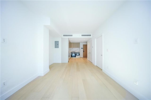 corridor with baseboards, light wood finished floors, visible vents, and electric panel