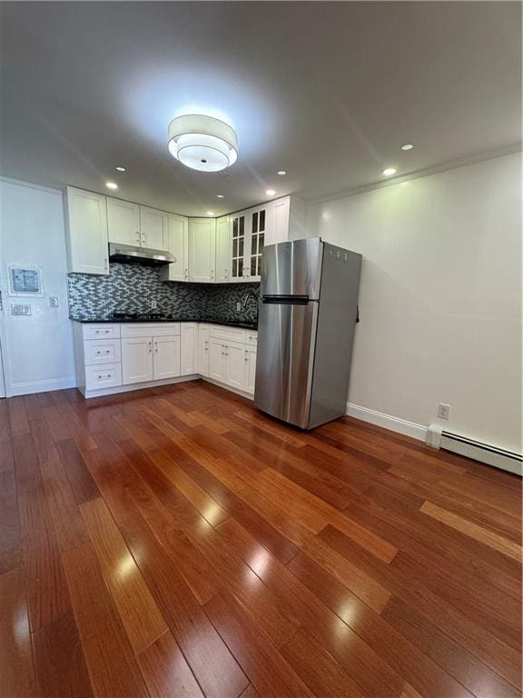 kitchen with under cabinet range hood, a baseboard heating unit, dark countertops, freestanding refrigerator, and decorative backsplash