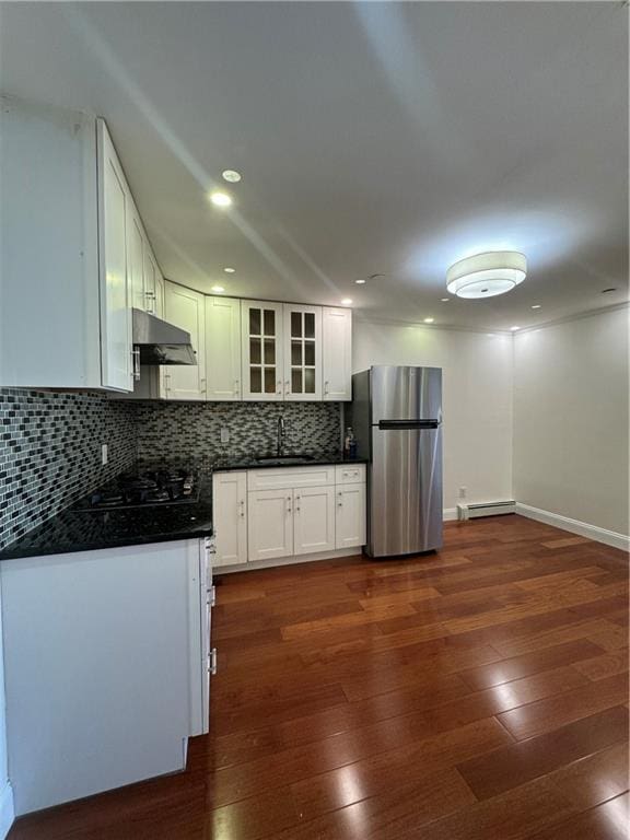 kitchen featuring under cabinet range hood, dark wood-type flooring, freestanding refrigerator, tasteful backsplash, and dark countertops