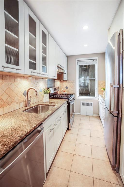 kitchen featuring sink, appliances with stainless steel finishes, radiator heating unit, light stone countertops, and white cabinets