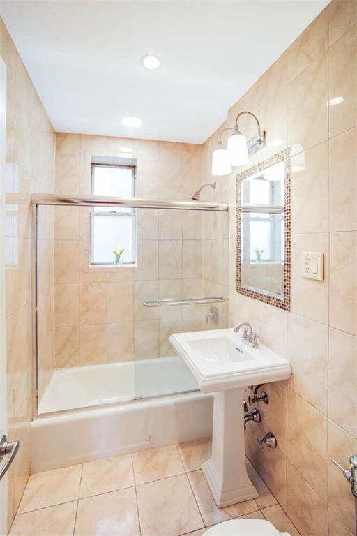 bathroom with tile patterned flooring, toilet, tile walls, and shower / bath combination with glass door