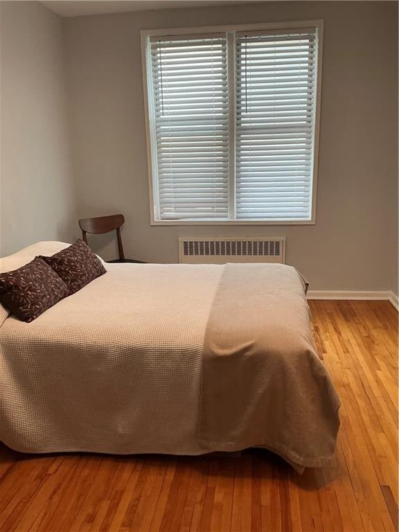 bedroom featuring hardwood / wood-style floors, radiator heating unit, and baseboards