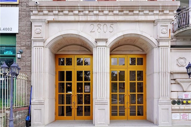 entrance to property featuring stone siding, french doors, and fence