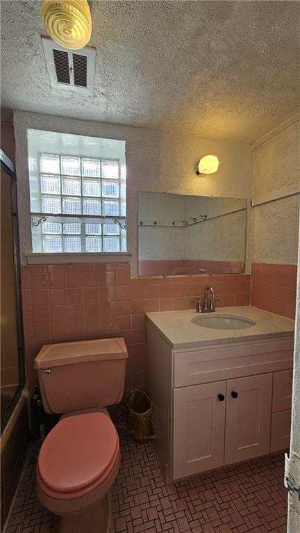 full bathroom featuring vanity, a textured ceiling, tile walls, and toilet