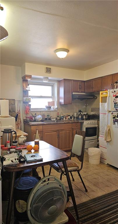 kitchen with visible vents, under cabinet range hood, dark countertops, white appliances, and decorative backsplash