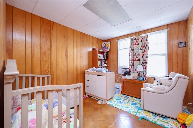 bedroom with parquet floors, a nursery area, and wooden walls