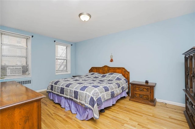 bedroom with radiator, light wood-style floors, and baseboards