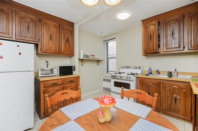 kitchen featuring light tile patterned floors, a sink, light countertops, white appliances, and radiator heating unit
