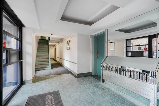 interior space with tile patterned flooring, a tray ceiling, stairway, and baseboards