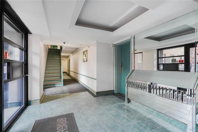 hallway featuring a tray ceiling, tile patterned floors, baseboards, and stairway