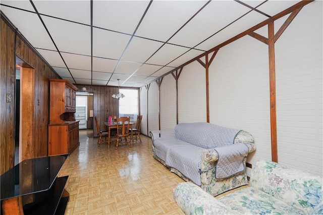 living room featuring light parquet floors, a drop ceiling, and wooden walls