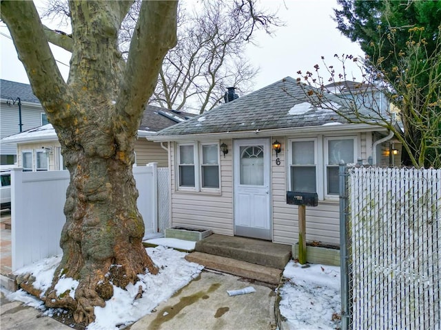 bungalow-style home featuring roof with shingles and fence