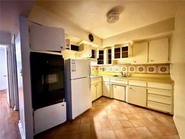 kitchen featuring white appliances, glass insert cabinets, light countertops, and a sink