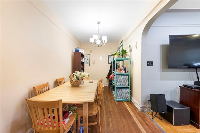 dining area featuring an inviting chandelier, arched walkways, baseboards, and wood finished floors