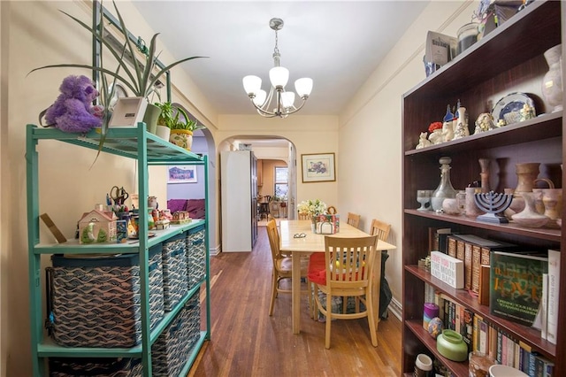 dining space with arched walkways, wood finished floors, and an inviting chandelier