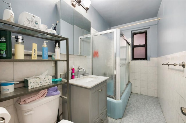 bathroom featuring toilet, an enclosed shower, vanity, tile patterned flooring, and tile walls