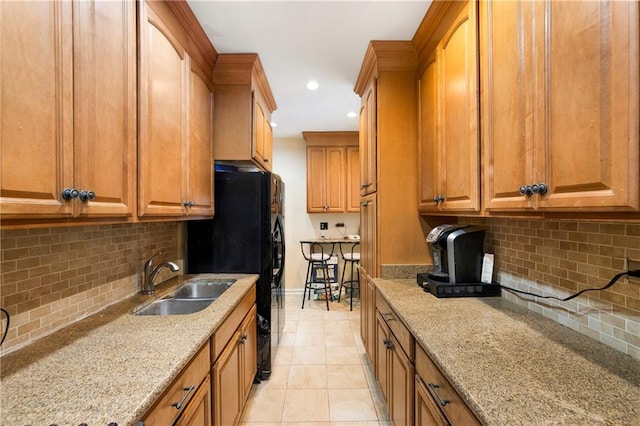 kitchen with recessed lighting, light tile patterned floors, a sink, light stone counters, and brown cabinetry