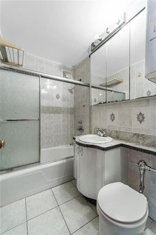 full bathroom with tile walls, vanity, bath / shower combo with glass door, toilet, and tile patterned flooring