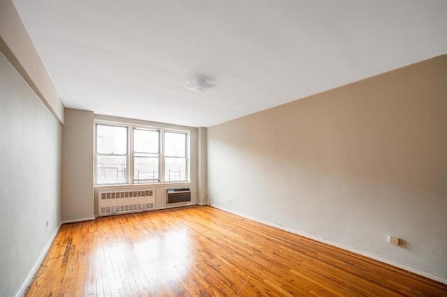 spare room with radiator heating unit, a wall mounted AC, light wood-style flooring, and baseboards