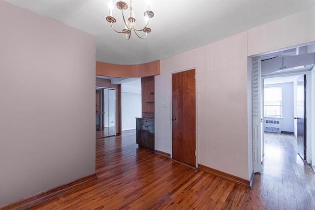 hallway with wood finished floors, a chandelier, radiator heating unit, and baseboards