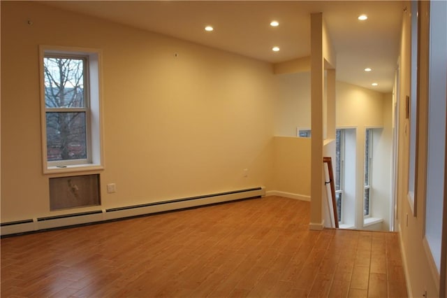 unfurnished room with a baseboard heating unit, vaulted ceiling, and light wood-type flooring