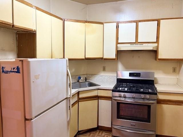 kitchen with stainless steel gas stove, under cabinet range hood, light countertops, a sink, and freestanding refrigerator