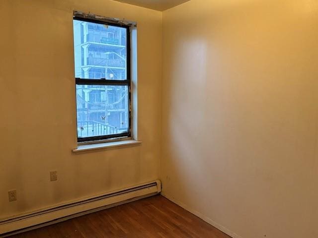 empty room with a baseboard heating unit, baseboards, and dark wood-style floors