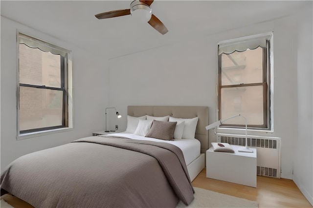 bedroom with a ceiling fan, radiator, and light wood finished floors