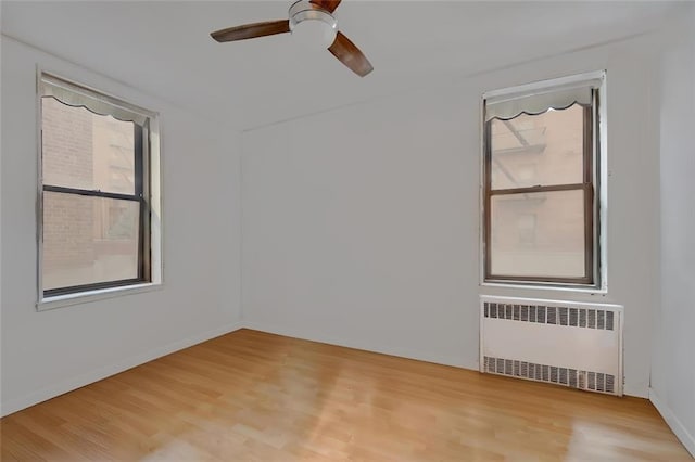 unfurnished room featuring a ceiling fan, light wood-type flooring, baseboards, and radiator heating unit