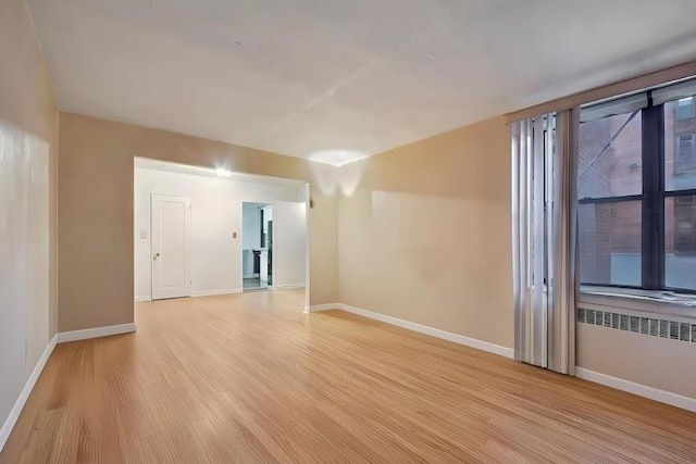 empty room featuring baseboards, radiator heating unit, and light wood-style floors