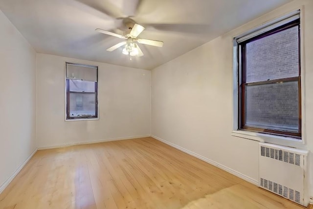 unfurnished room with radiator, light wood-style flooring, baseboards, and a ceiling fan