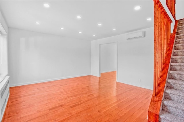 unfurnished living room featuring light wood-type flooring, a wall unit AC, stairs, and recessed lighting