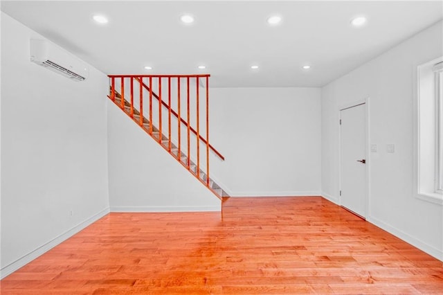 unfurnished room with recessed lighting, a wall mounted AC, light wood-type flooring, baseboards, and stairs